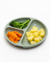 Divided green plate with carrots, broccoli, and pineapple on a white background