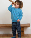 Child wearing a blue sweater and checkered pants, standing on a wooden floor.