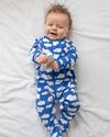 Baby wearing a blue onesie with white cloud patterns, lying on a white surface.