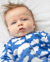 Baby wearing a blue onesie with white cloud patterns on a white background