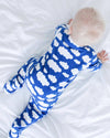 Child wearing a blue onesie with white cloud patterns on a white bed.