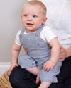 Baby wearing a blue striped romper sitting on a person's lap.