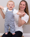 Woman holding a baby wearing blue striped overalls against a plain background