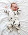 Newborn baby wearing a white onesie with black giraffe patterns, lying on a white surface.