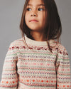 Child wearing a patterned sweater against a gray background