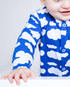Baby wearing a blue onesie with white cloud patterns on a plain background