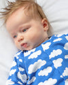 Baby wearing a blue onesie with white cloud patterns on a white background
