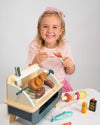 Child playing with a toy hot dog stand and utensils on a white surface.