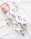 Baby sleeping in a white onesie with black penguin pattern on a white blanket