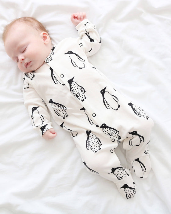 Baby sleeping in a white onesie with black penguin pattern on a white blanket
