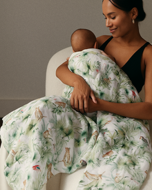  Woman holding a baby wrapped in a green and white patterned blanket on a couch.