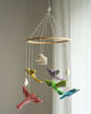 Colorful bird mobile hanging from a wooden ring against a neutral background