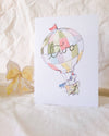 Greeting card with hot air balloon design and 'hello' text on a textured surface.
