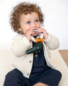 Child wearing a beige knit cardigan holding a toy with a white background