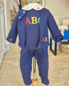 A navy blue baby jumpsuit with colorful embroidered letters 'ABC' on the chest and a small red apple detail on the sleeve, displayed on a mannequin in a retail store.