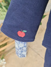 Close-up of a navy blue ribbed knit sleeve featuring a small embroidered red apple with a green leaf on the cuff.