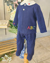 A navy blue baby footed sleeper with a white collar and colorful embroidered letters 'ABC' on the chest, displayed on a mannequin torso.