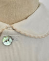 Close-up of a cream knit garment with a wide cream collar and a round iridescent shell button, shown on a mannequin torso.