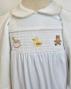 A white baby smocked dress with a Peter Pan collar and embroidered toy motifs (a rocking horse, a yellow duck, and a teddy bear) across the chest, displayed on a mannequin torso.