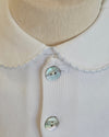 Close-up of a cream-colored ribbed knit top with a wide flat collar and two mother-of-pearl buttons, displayed on a mannequin torso.