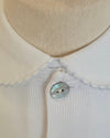 Close-up of a cream-colored knit cardigan featuring a wide, scalloped collar and a single mother-of-pearl button.