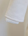Close-up of a white ribbed knit sleeve or cuff with a folded hem showing a light blue scalloped edge.