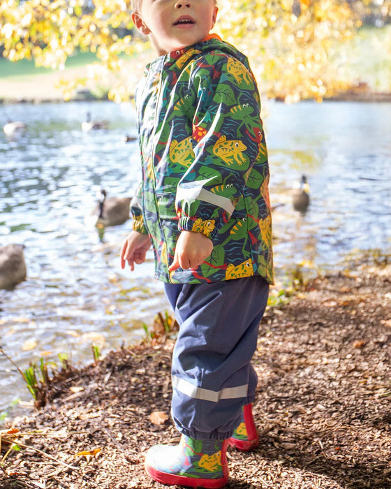 Child wearing a colorful raincoat by a lake with ducks