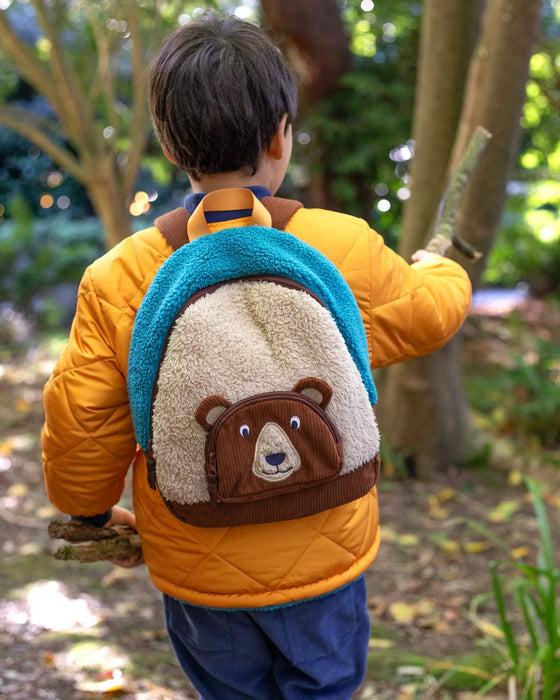 Child wearing a yellow jacket with a bear-themed backpack in a forest setting