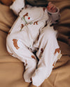 Baby in a white onesie with brown bear prints lying on a brown blanket