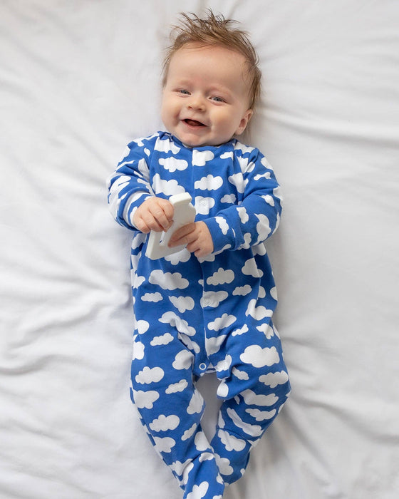 Baby wearing a blue onesie with white cloud patterns, lying on a white surface.