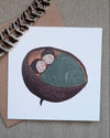 Card with illustration of two people in a shell, feather, and envelope on a textured surface