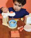 Child playing with a wooden toy kitchen set on a wooden table.