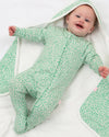Baby in a green floral onesie lying on a white blanket