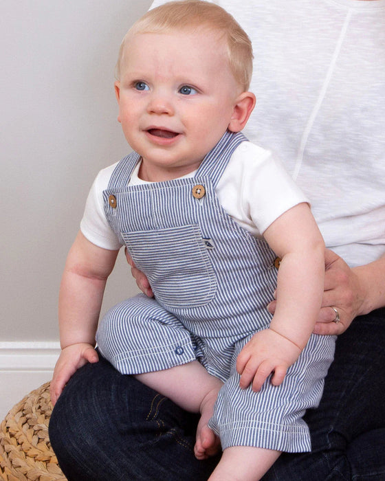 Baby wearing a blue striped romper sitting on a person's lap.
