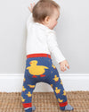Baby wearing blue leggings with yellow duck patterns on a white background