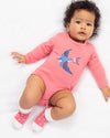 Baby wearing a pink onesie with a blue bird design on a white background