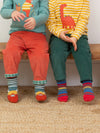 Two children sitting on a wooden bench wearing colorful clothing and socks.
