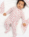 Baby in a floral onesie lying on a white blanket with floral patterns.