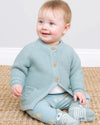 Baby wearing a light blue knitted cardigan and matching pants sitting on a beige carpet.