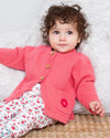 Baby wearing a pink knitted cardigan on a textured surface