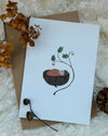 Greeting card with a nature-themed illustration on a textured surface with dried flowers and a pine cone.