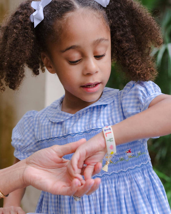 Young girl in a blue checkered dress with pigtails, interacting with another person outdoors.