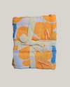 Folded fabric with orange and blue pattern tied with a beige ribbon on a light gray background