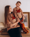 Woman and child in matching brown sweaters with fox designs, holding a red fox plush toy.