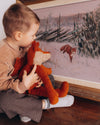 Child holding a stuffed animal in front of a painting of a fox