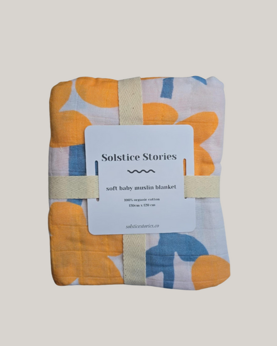 Baby muslin blanket with colorful patterns and a 'Solstice Stories' label on a light gray background