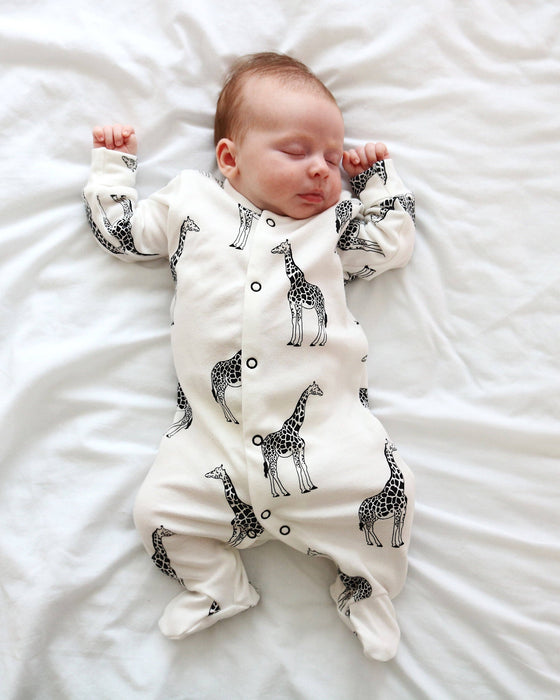Newborn baby wearing a white onesie with black giraffe patterns, lying on a white surface.