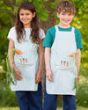 Two children wearing aprons with carrot designs outdoors.