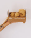 Box of 'My First Bunny' plush toys held by a hand with a tattoo on a white background