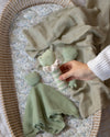 Hand holding a green baby rattle near a crib with a blanket and baby comfort blanket.